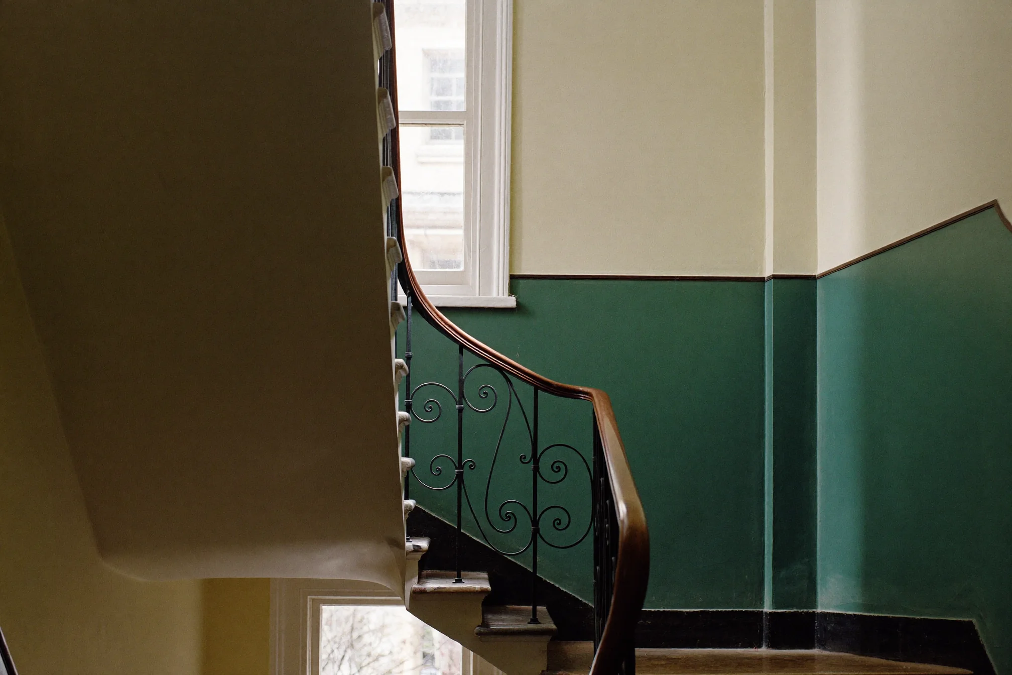 Klatka schodowa kamienicy z kutą balustradą i zieloną lamperią